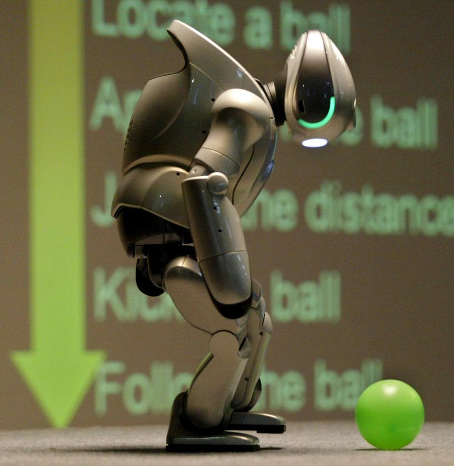 The robot is bent over at the neck, looking at its feet. Slightly in front of it is a green ball.