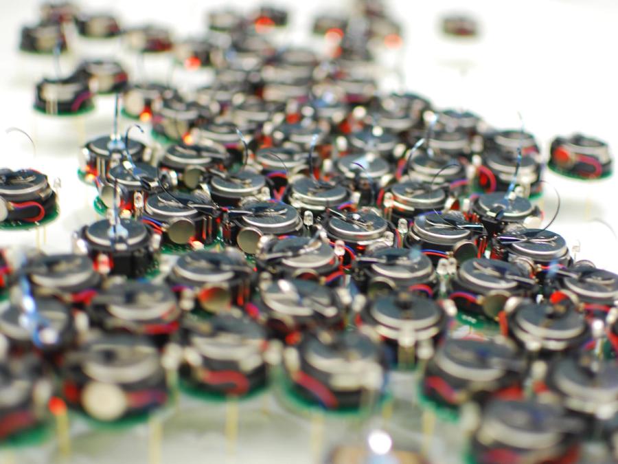Close-up shows about 75 small kilobot robots gathered together.