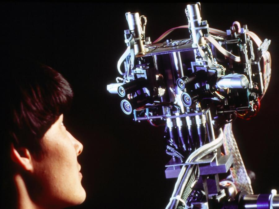 Close up of a woman and robot staring at each other.