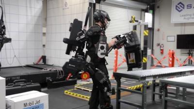 A man wearing the Guardian XO full-body exoskeleton suit lifts a heavy case at a test lab.