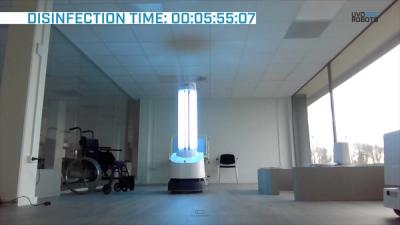 A tall robot carrying bright UV lights drives around a hospital room furnished with chairs, seats, and tables.