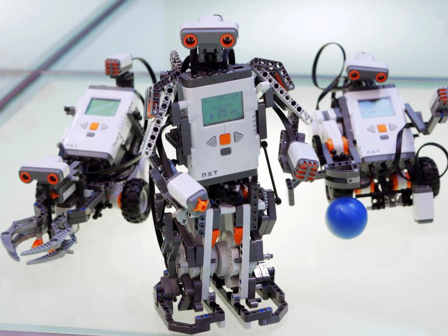 A humanoid robot made of Lego bricks, with a programmable module for a torso. behind it are two other shapes for the robot.