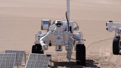 GITAI's G1, a humanoid robot with a while metal body, camera-packed head, and rover-like wheel base, handles solar panels in a desert-like area that simulates the lunar environment.
