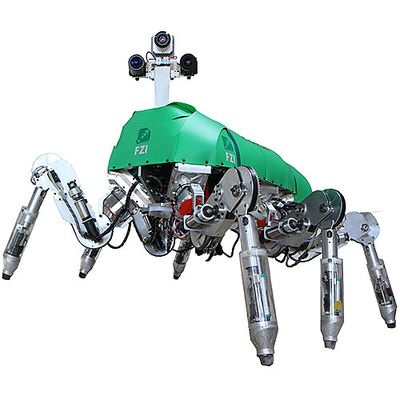 The robot has six metallic jointed legs, a green shell base and a mast with three cameras for a head. 