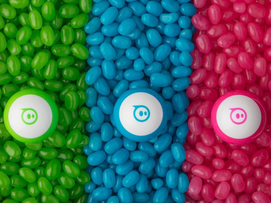 Three piles of colorful jellybeans, each with a color matching Sphero mini on top, in green, blue, and pink.