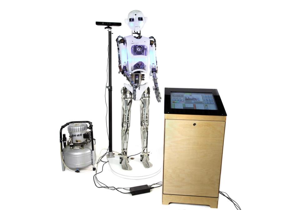 The humanoid robot stands on a platform next to a podium with a display and other equipment.
