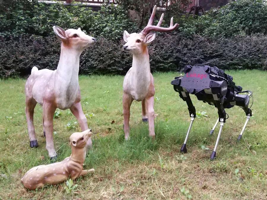The robot stands among 3 fake lawn deer.
