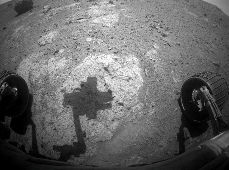 Black and white image shows a photo taken by Opportunity in which two of its wheels, and the shadow of its head are seen.