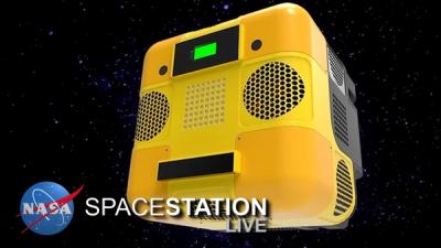 A 3D rendered yellow cubic robot with displays, lights, and air vents floats in space against a background of stars with the NASA logo on the lower left corner.