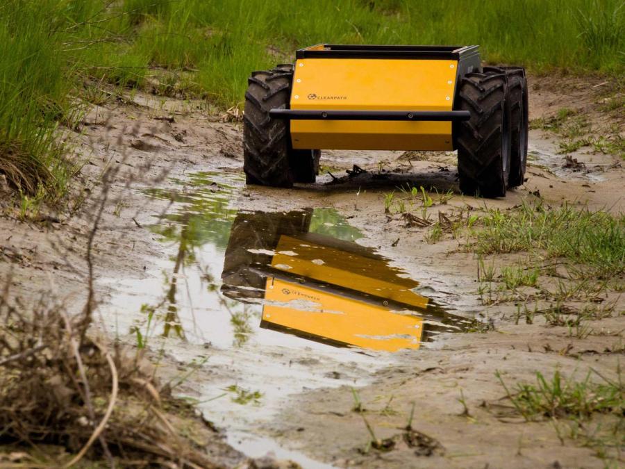 Yellow and black wheeled vehicle is seen driving through, and reflected in, mud.