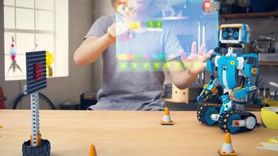 A young boy interacts with a virtual app interface to control a small humanoid robot built with Lego Boost blocks.