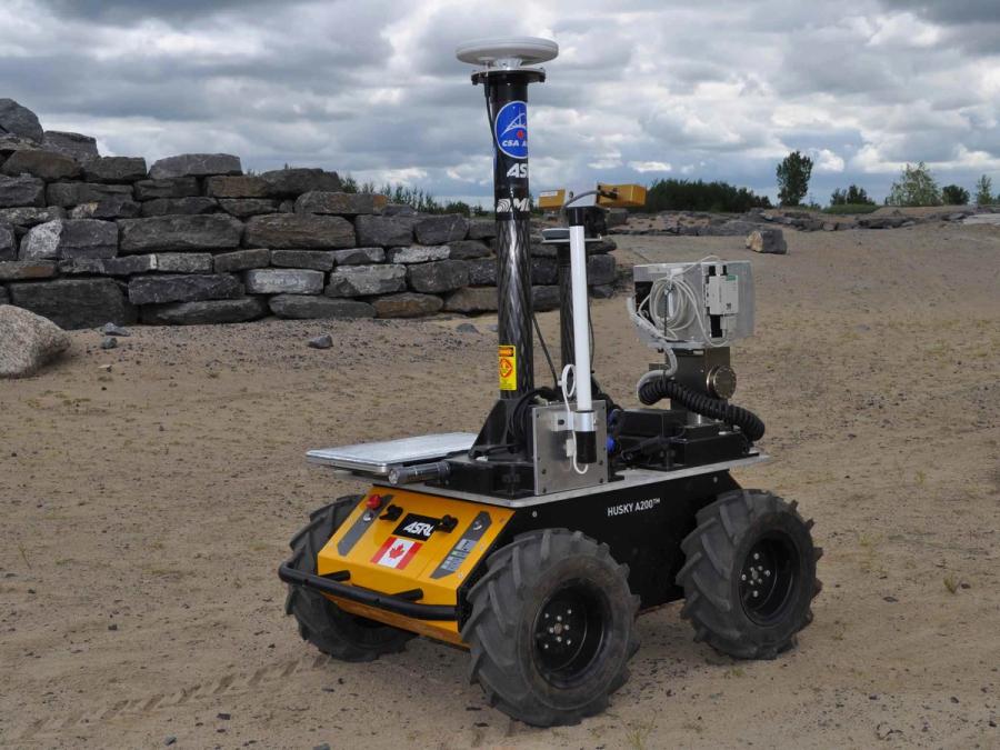 The vehicle has been adapted to carry a large silver plat holding tall equipment and sensors. It is driving through a sandy environment.