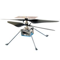 A small in-flight helicopter with a square silver body the size of a tissue box, a pair of carbon fiber rotors, a rectangular solar panel on top, and four spindly legs on the bottom.