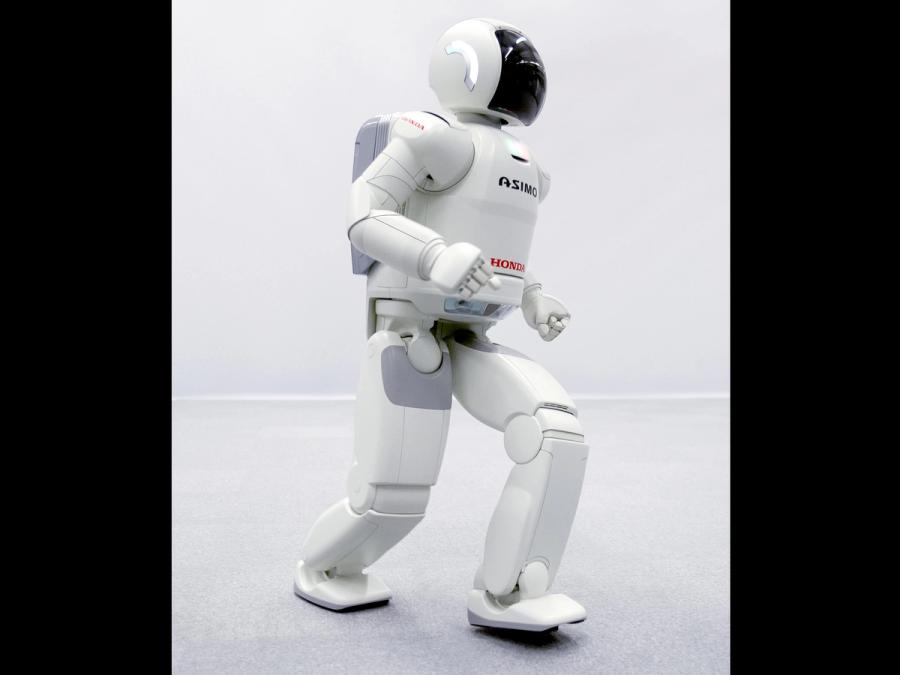 The two legged, white Asimo robot takes a step.