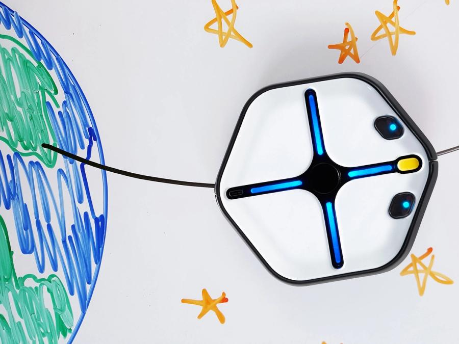 A squat white hexagon with a black circle, glowing blue lines, yellow button nose and two blue glowing eyes moves on a whiteboard with a drawing of the Earth and stars.