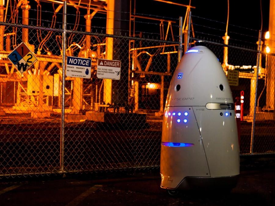 A rocket shaped rolling robot with glowing blue lights stands outside a substation.