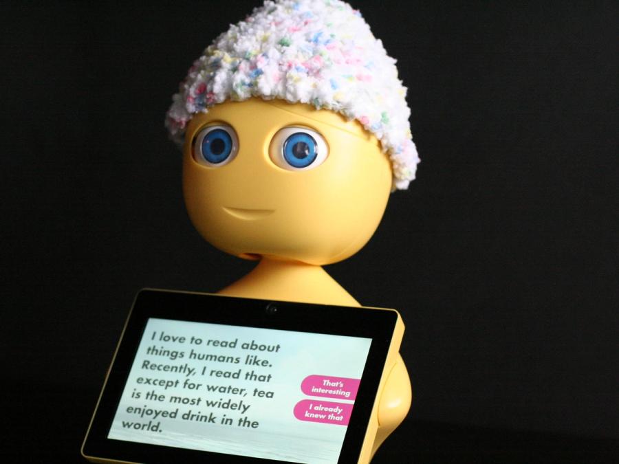 The little robot wears a knit cap and holds a tablet that says "Recently, I read that except for water, tea is the most widely enjoyed drink in the world." 