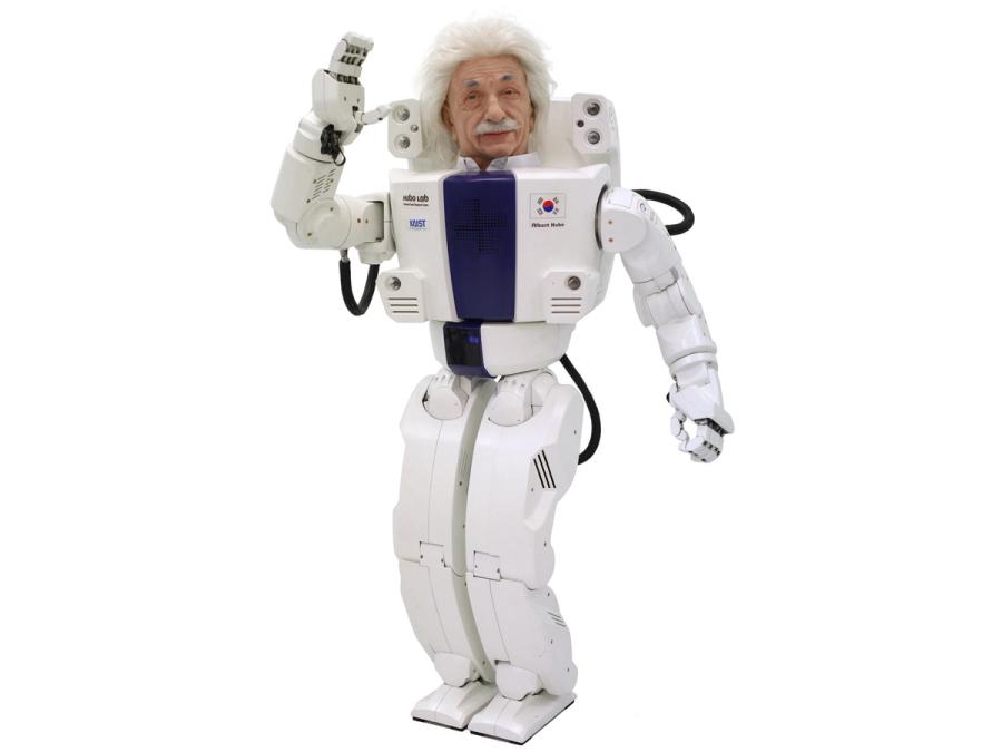 A male humanoid robot with fluffy white hair and a mustache in the style of Albert Einstein waves.