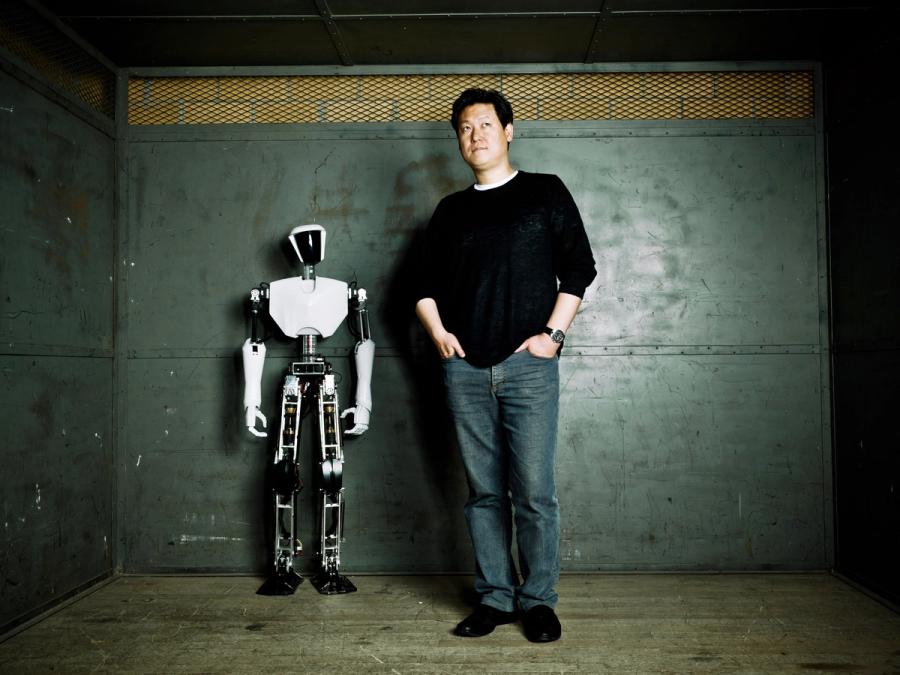 A man in black shirt and jeans stands next to a white and black humanoid robot that is as tall as his chest.