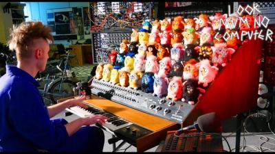 A musician and maker plays a keyboard that controls 45 Furbys.