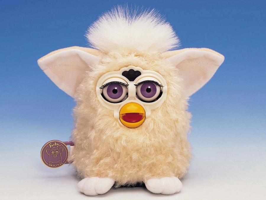 Furby is a fluffy white owl-like toy with large purple eyes, a yellow beak, pointy ears and a white fluff on top of its head.