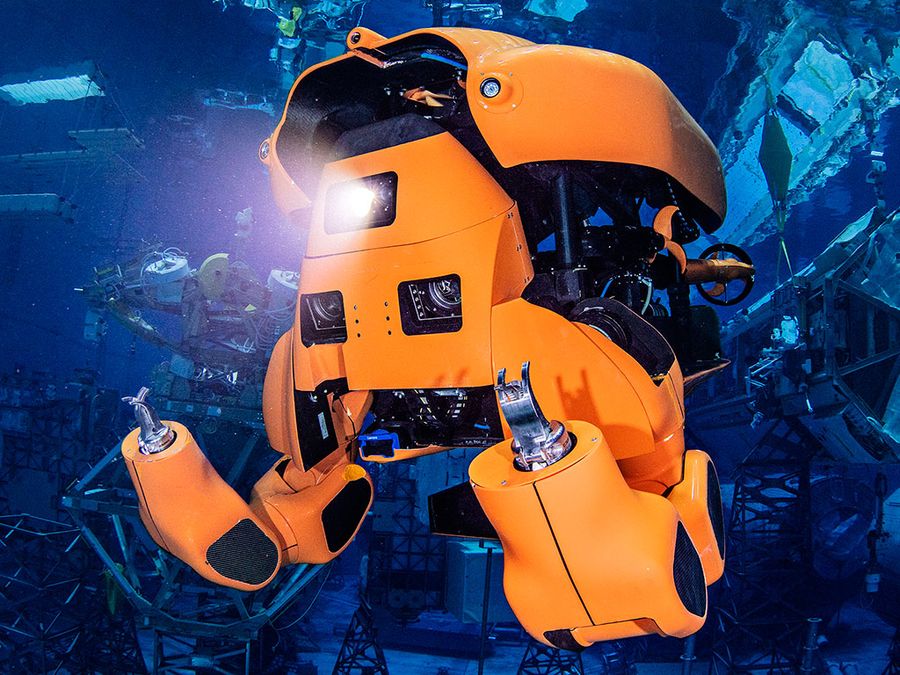 Aquanaut, an orange humanoid transforming robot, shines a light and floats underwater.