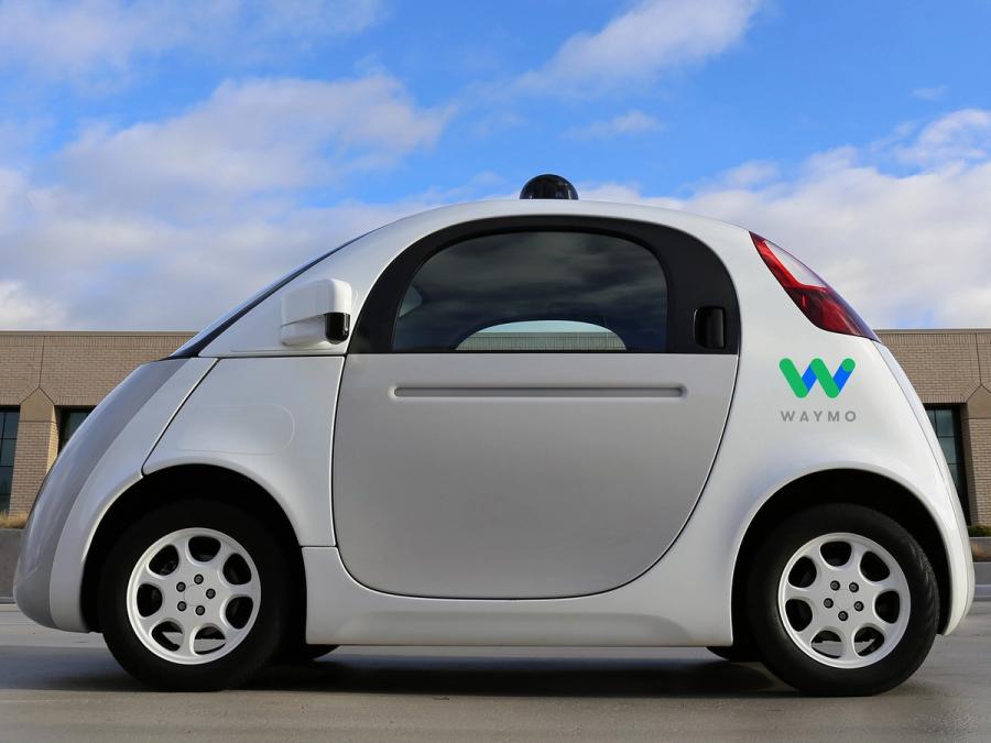 A white and gray compact car with small black dome on top and reads "Waymo" on side.