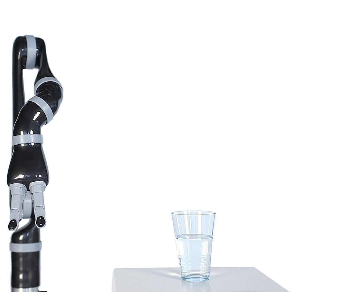 A black and grey robotic arm with a three finger gripper moves to pick up a glass of water, and then put it back down.