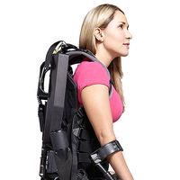 A blonde woman in a pink shirt wears a black exoskeleton backpack suit, and crutches on her arms.