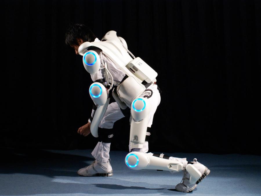 A person in a lunge position shows off a full body white exoskeleton with blue circular lights at the joints.