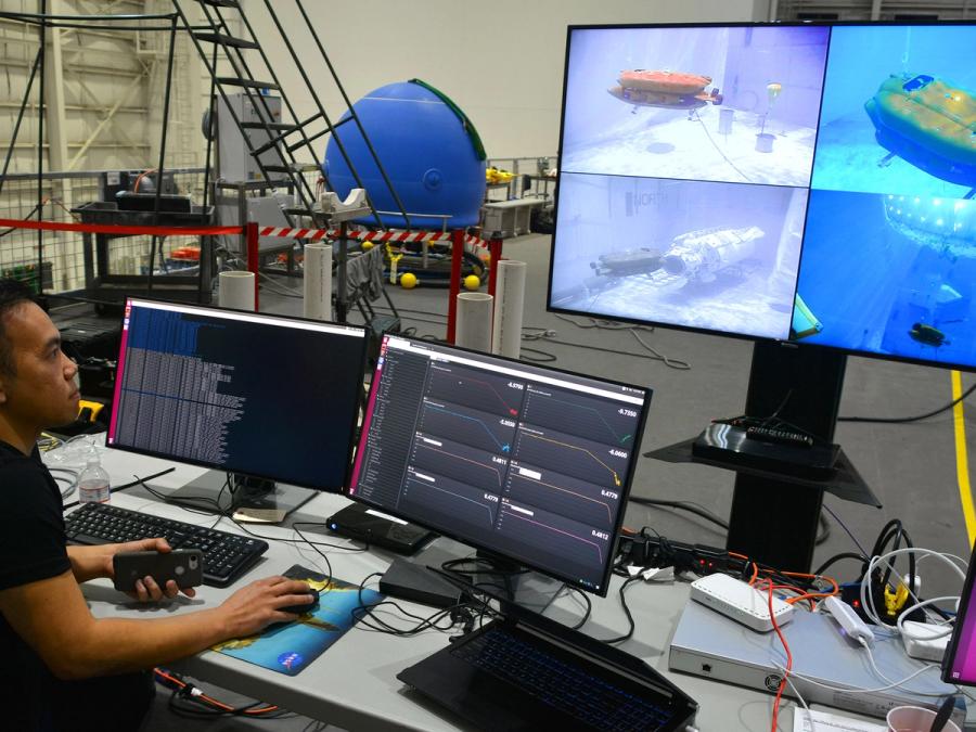 An engineer looks a four computer screens showing images and data from a submarine robot.