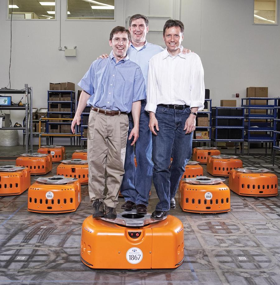 Three men balance on an orange robot while many of the same robot are lined up behind them.