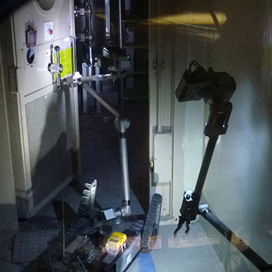 PackBot with tracked wheels and long extension arm opens a door in a dark building.