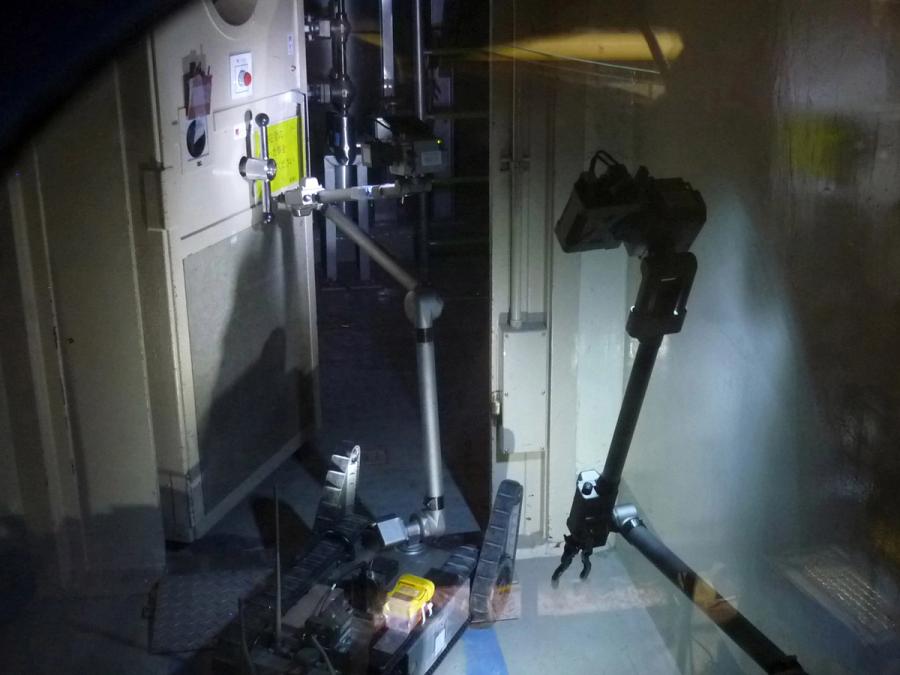 Two wheeled robots with long extension arms open a door in a dark building.