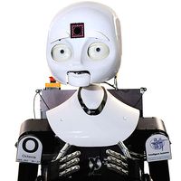 The robot has an expressive white face with eyes, nose, mouth, and a glowing square in its forehead. The robot has two arms with jointed human like silver fingers.