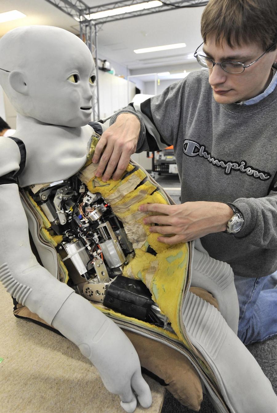 A man in glasses holds open the side of the robots "skin" to show the electronics within.