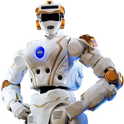 A high-tech humanoid stands in a power pose with hands on its hips. It's appearance resembles an astronaut, with its white jointed body, helmet with gold accents, and chest plate with the NASA logo.
