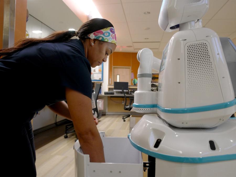 A nurse reaches her hands into a drawer that opens from the robot's mobile base torso.
