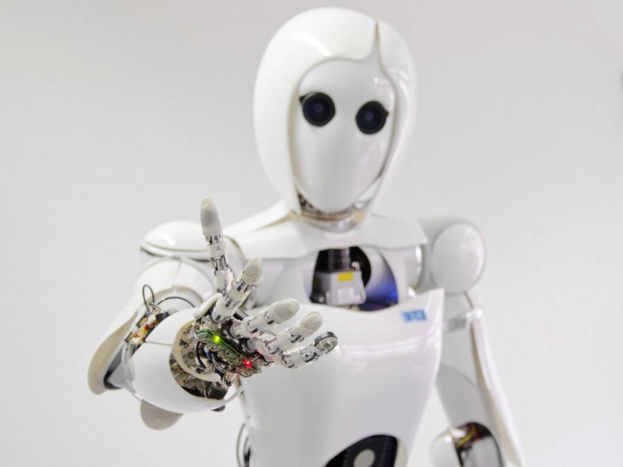 A white humanoid robot reaches a hand towards the camera.
