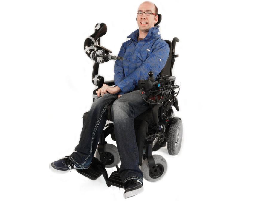 A smiling man in a wheelchair with a robotic arm attachment.