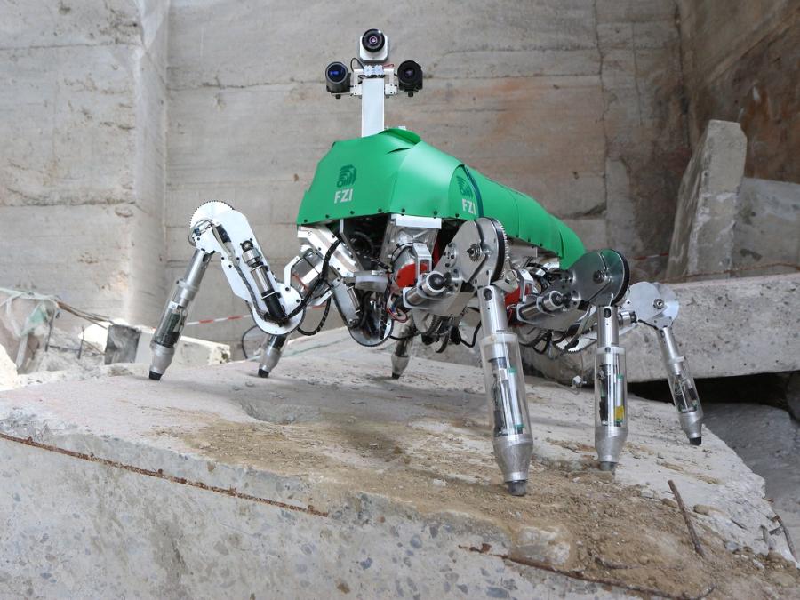 The robot has six metallic jointed legs, a green shell base and a mast with three cameras for a head.