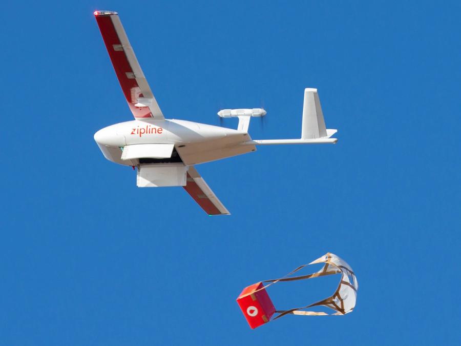 The aircraft in flight drops a red package attached to a parachute.