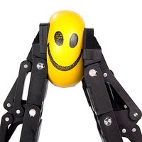A pair of black robotic gripper fingers smush a yellow smiley face ball.