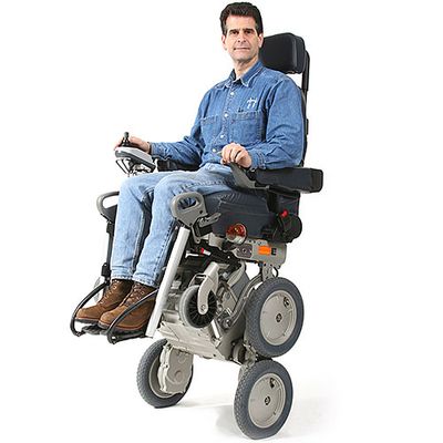 A man clothed in denim shirt and jeans sits in a robotic wheelchair that is elevated on two of it's four main wheels.
