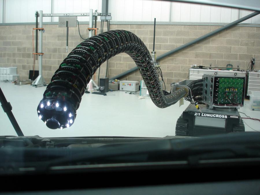 A long, tightly segmented robot with lights and camera on it's end protrudes from a large treaded tank base to inspect wires in the distance.
