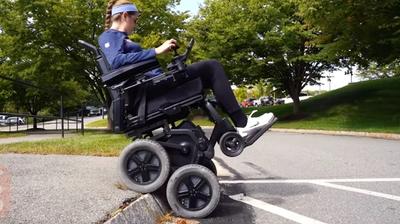 A woman sitting on an iBOT powered wheelchair goes down a curb.