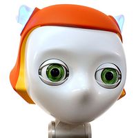 Close up of a robots head. The robot has an orange headpiece, glowing blue cat ears and large green eyes.