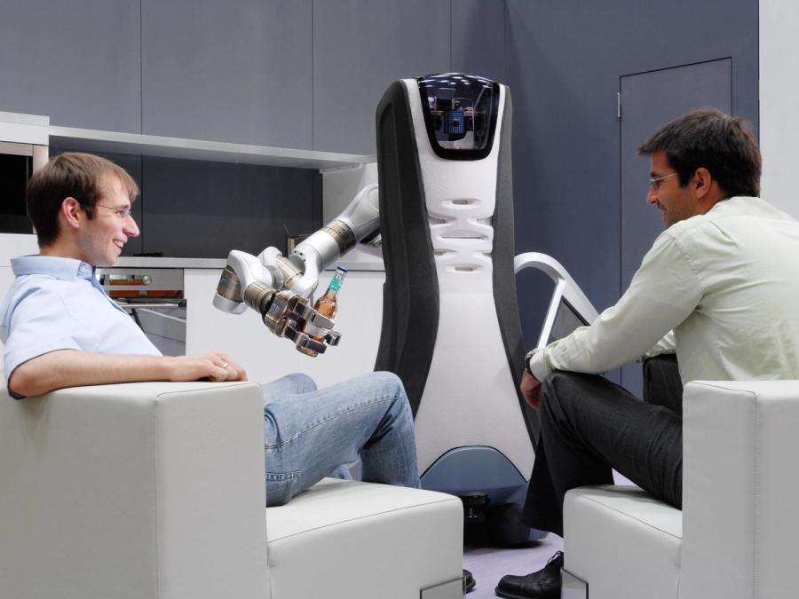 A robot holds a beer out to one of two seated men.