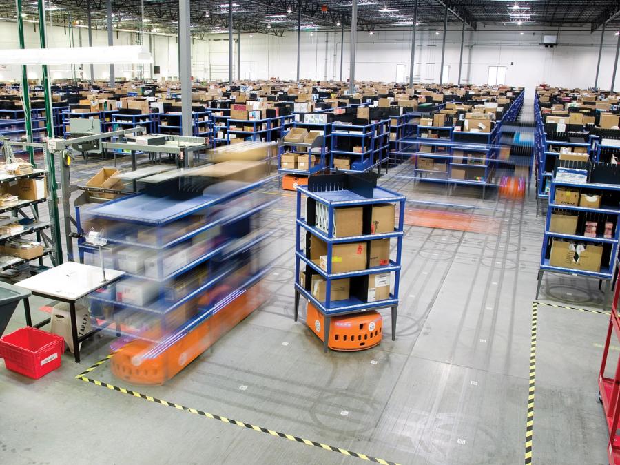 A warehouse full of orange robots zipping around while carrying multi-tiered shelves of boxes and items.