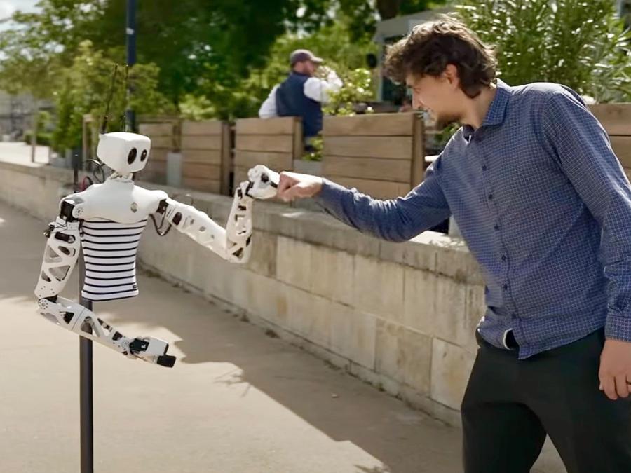 The robot and a man in a blue shirt give each other a fist bump while outdoors.